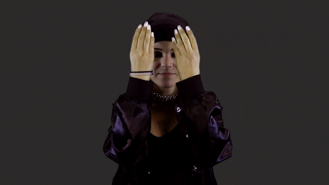 Sem estresse Em fundo preto, vemos uma jovem de olhos fechados, da altura do busto para cima. Ela está fazendo um movimento com os braços como se tivesse puxando algo com as mãos de cima para baixo. O ato lembra um movimento comum entre pessoas que meditam.