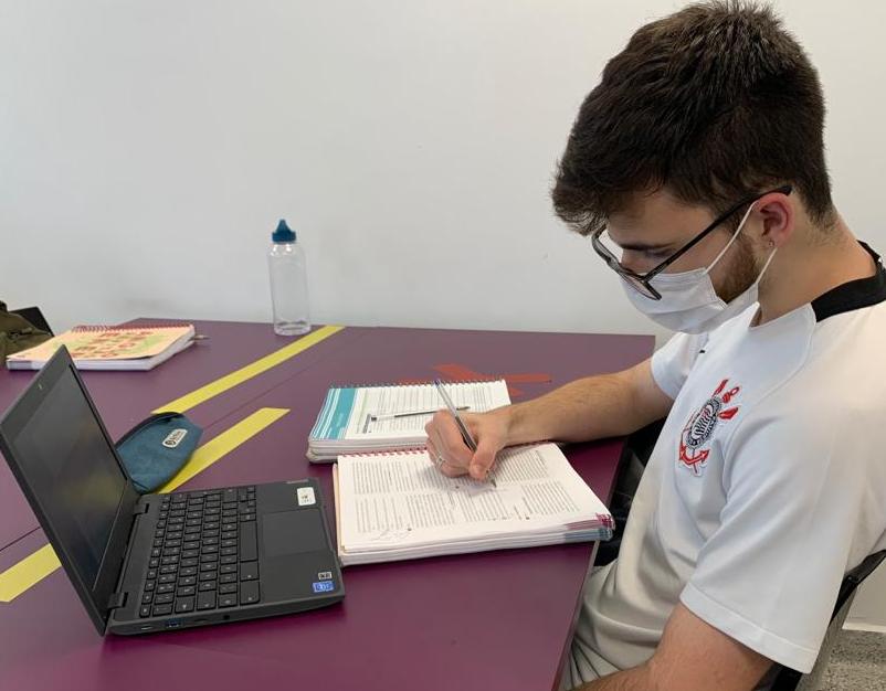 Luís Henrique Amaral Silva Estudante Luís Henrique Amaral Silva está em uma mesa com notebook, caderno e garrafa de água. Ele usa máscara e camiseta do Corinthians.