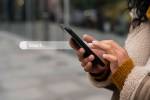 Pessoa segurando celular. Há uma interevenção artística com a barra de pesquisa do buscador ao lado do celular.