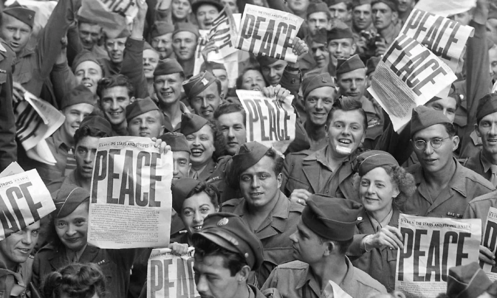 População se amontoa celebrando fim da guerra, seguram jornal que estama 