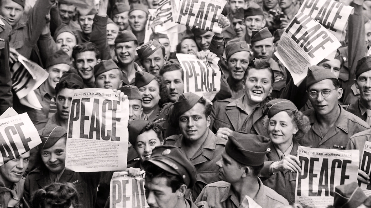 Soldados e civis comemoram fim da guerra nas ruas, segurando jornal que diz PEACE ("paz")