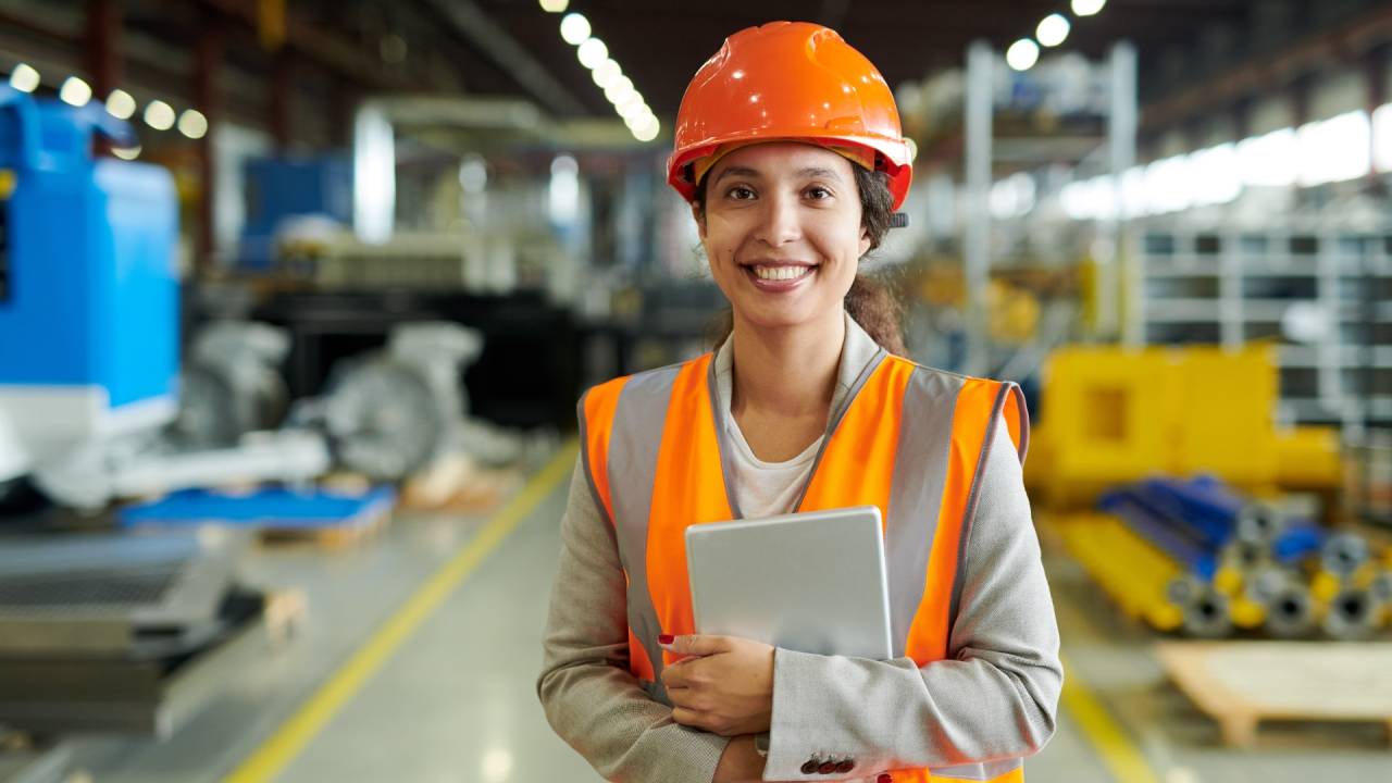 mulher em uma fábrica com capacete sorrindo